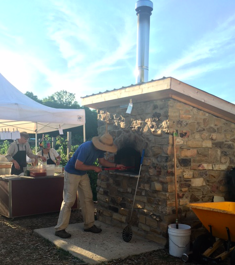 Troy Community Farm employee takes hot pizzas from the stone oven on Farm Fresh Pizza Night. (Laura Schmitt/Madison Commons)