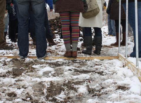 Conference participants stand on the skeleton of a hoop house to stay dry on a tour of the Goodman Community Center gardens.