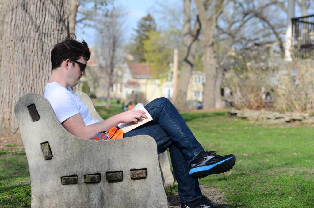 Adam King, a first-time visitor to Orton Park, reads a book while sitting on a bench along the park’s central pathway in Madison, Wis. on May 9, 2022.