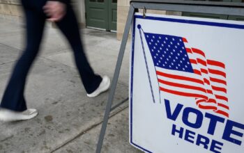 Pedestrians walk past a “Vote Here” sign at the entrance to the Memorial Union at the University of Wisconsin–Madison