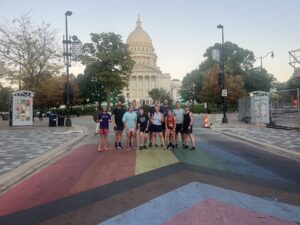 Runners in front of the Capitol with the LGBTQ+ flag painted on the street.