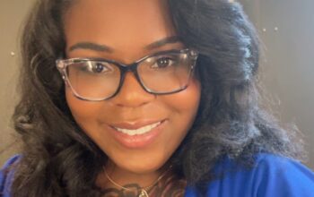 A Black woman with long black hair in a blue sweater smiles