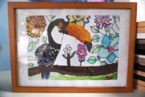 A black and orange toucan bird sitting on a brown tree with blue and purple flowers