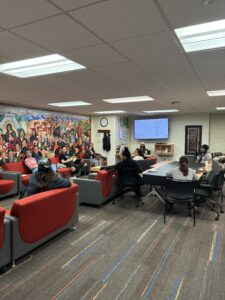 A grey carpet with red chairs in a room with a diverse population of UW-Madison students.