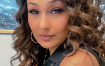 A Brown woman with long curly brown hair looks at the camer.