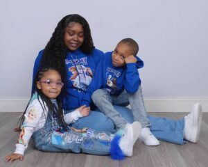 A Black woman in blue holds two Black kids.
