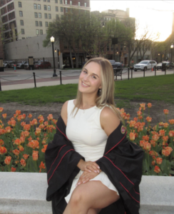 A young blonde woman with a white dress and a graduation gown.